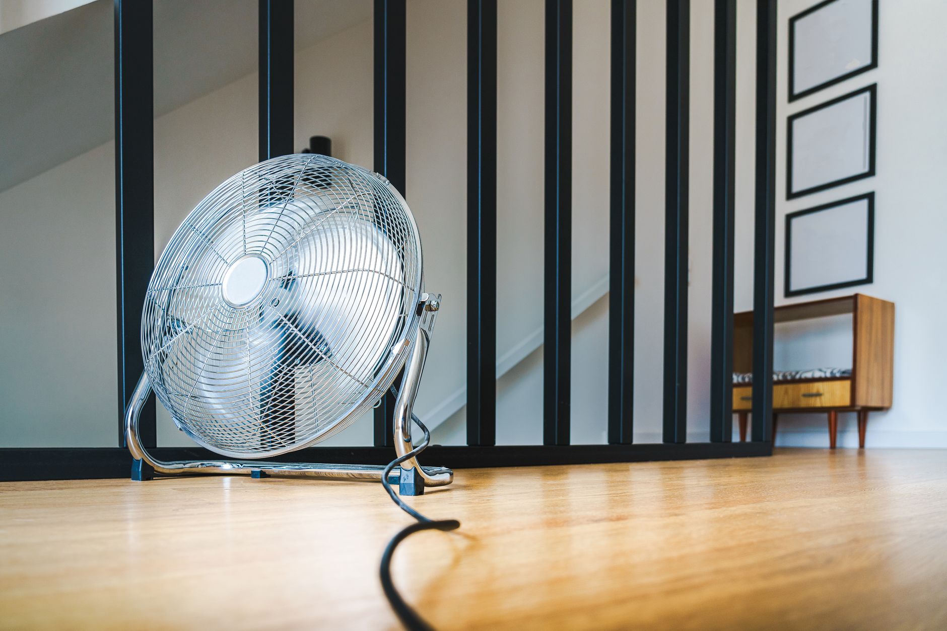 A sleek electric fan placed on a wooden floor in a modern indoor setting, providing comfort and cooling.