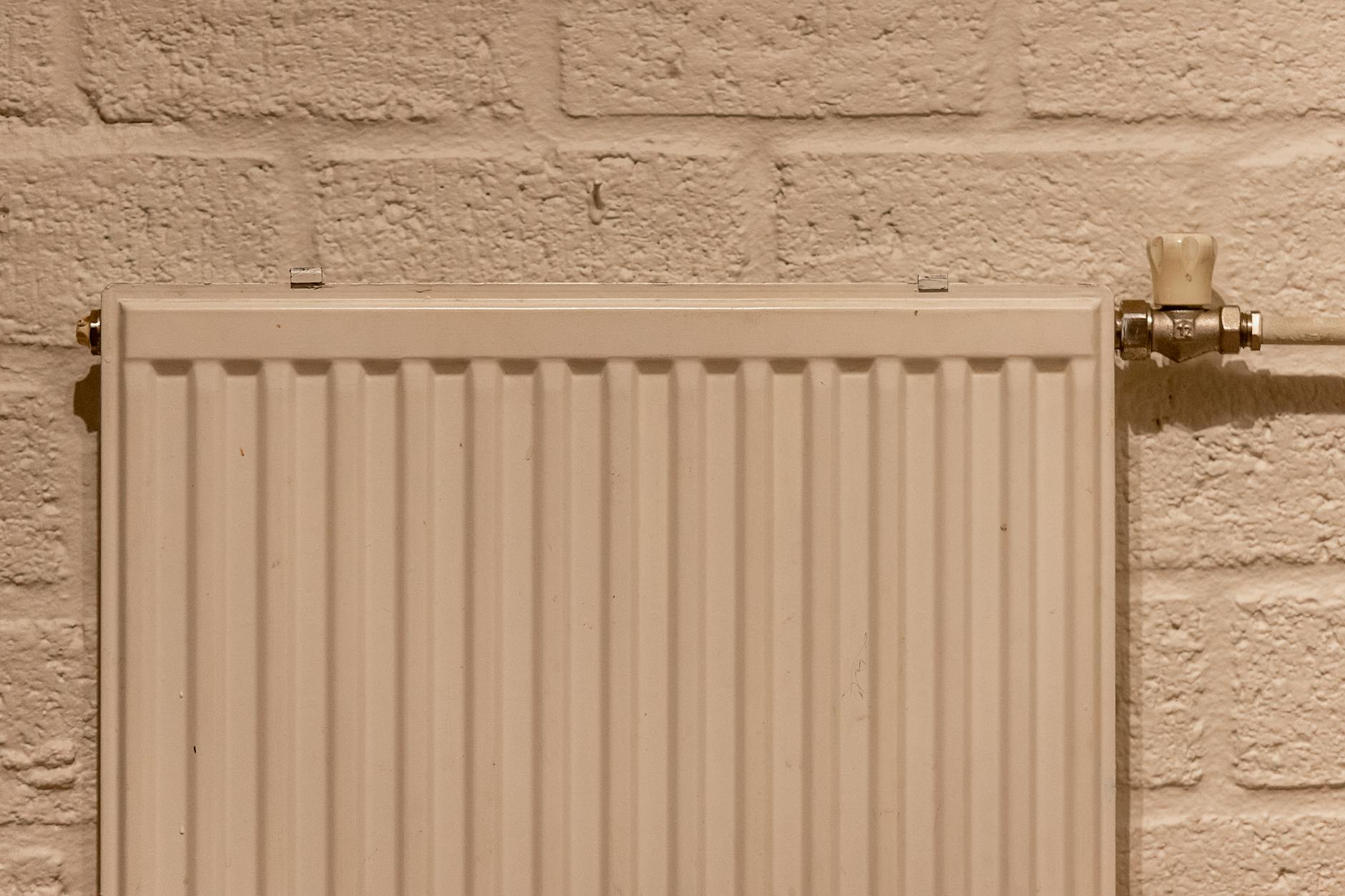 A clean white radiator mounted on a textured brick wall, indoors and well-lit.