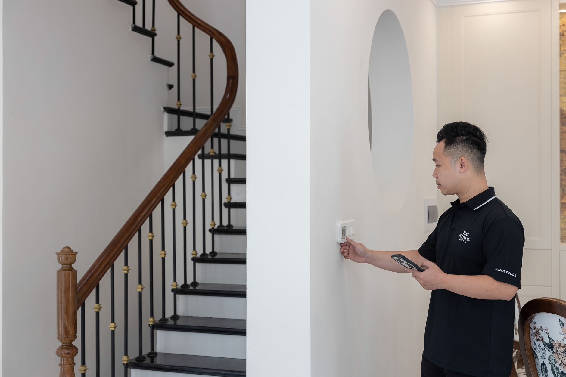 Man adjusting thermostat in stylish home with elegant staircase.