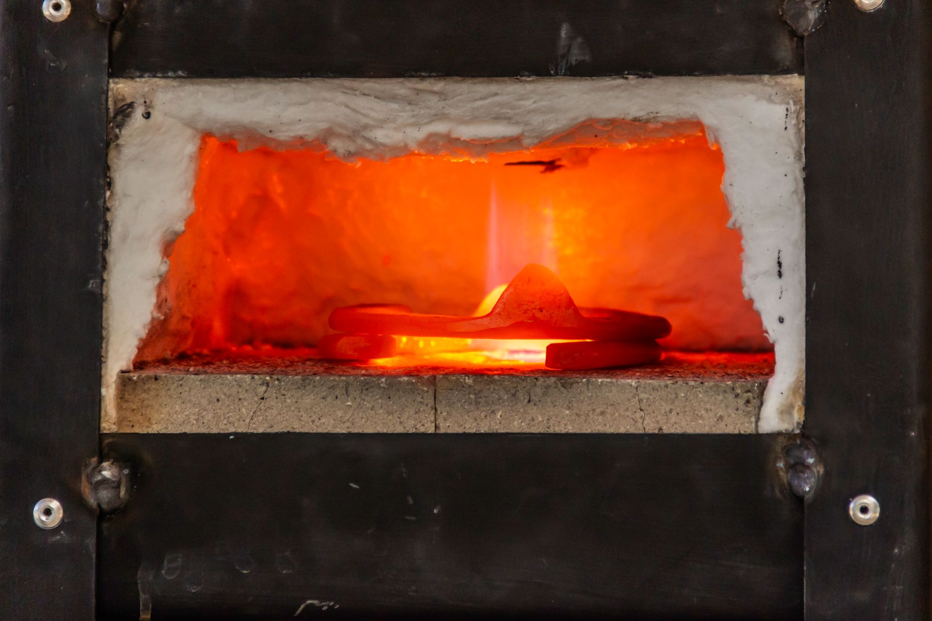 A close-up view of an industrial furnace with glowing metal heated inside, showing intense heat.